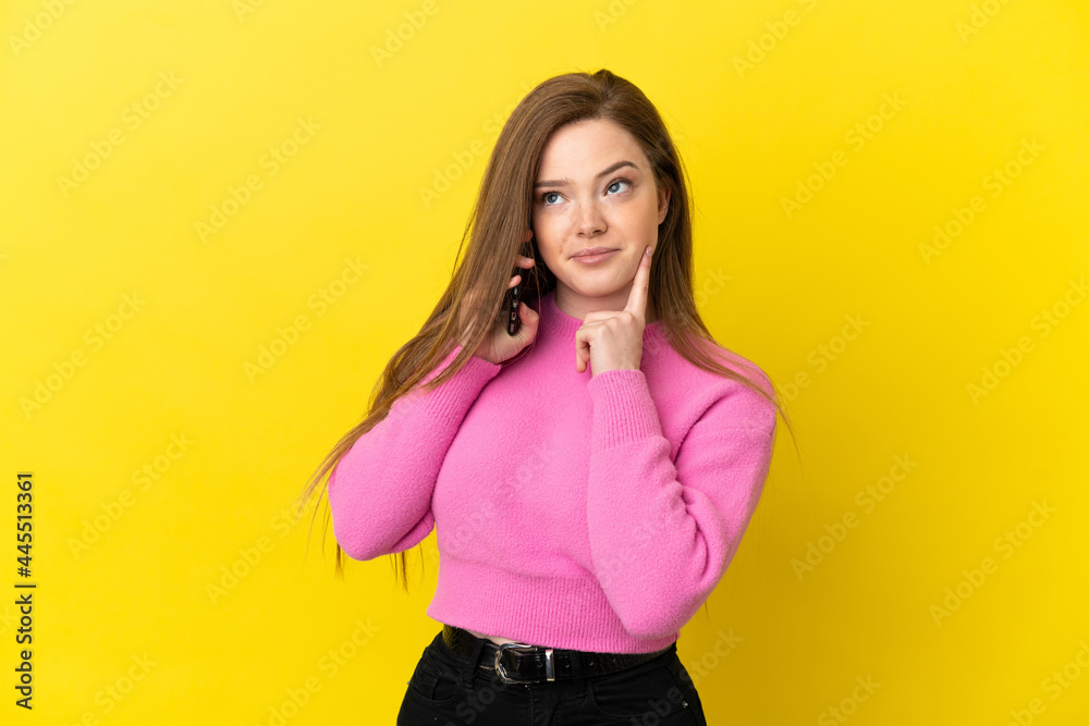 Teenager girl using mobile phone over isolated yellow background thinking an idea while looking up
