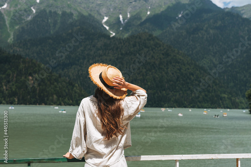 Young woman traveler with long blonde hair in straw hat looks at beautiful view of the mountain lake, people from behin photo