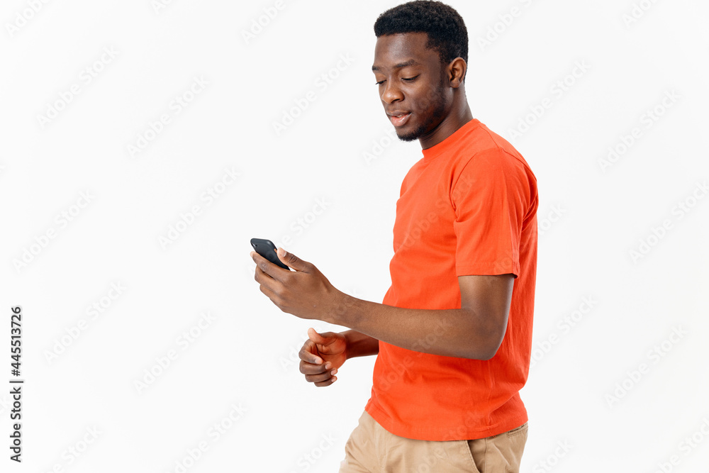 handsome african man with mobile phone on light background and orange t-shirt shorts handsome african man with mobile phone on light background and orange t-shirt shorts