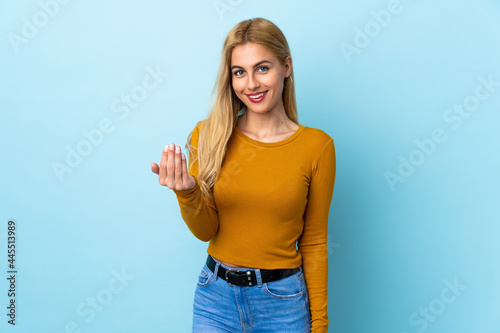 Young Uruguayan blonde woman over isolated blue background inviting to come with hand. Happy that you came