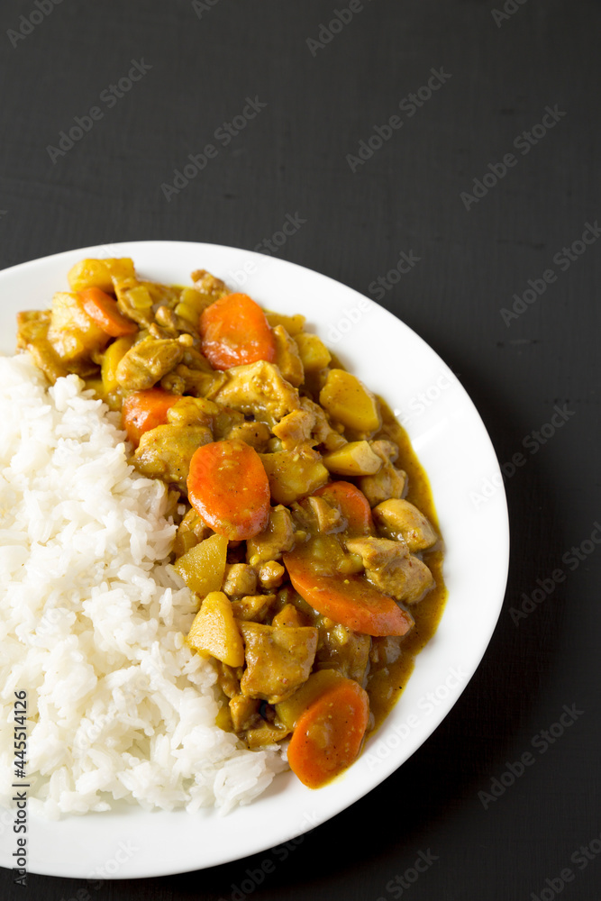 Homemade Japanese Chicken Curry on a white plate on a black background, side view. Copy space. Homemade Japanese Chicken Curry on a white plate on a black background, side view. Copy space.