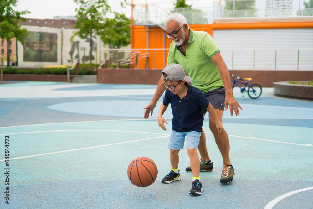 A happy little boy is playing basketball with his grandfather.