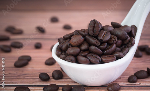 Close up heap of organic coffee beans in white ceramic bowl on wooden table.Selection of roasted brown coffee beans seed.