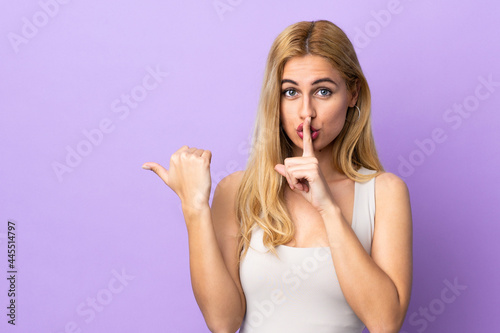 Young Uruguayan blonde woman over isolated background pointing to the side and doing silence gesture