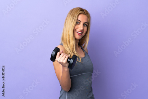 Young blonde sport woman making weightlifting over isolated purple background with happy expression