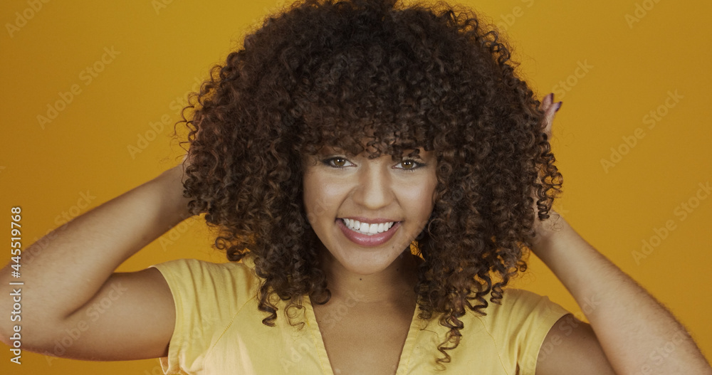 Fototapeta premium Happy laughing American African woman with her curly hair on yellow background. Laughing curly woman in sweater touching her hair and looking at the camera.