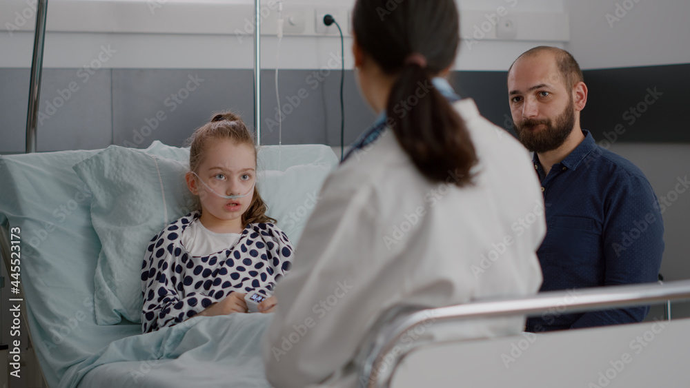 Pediatrician doctor discussing sickness treatment with sick patient and father during disease medicine examination in hospital ward. Hospitalized child lying in bed recovering after medical surgery Pediatrician doctor discussing sickness treatment with sick patient and father during disease medicine examination in hospital ward. Hospitalized child lying in bed recovering after medical surgery