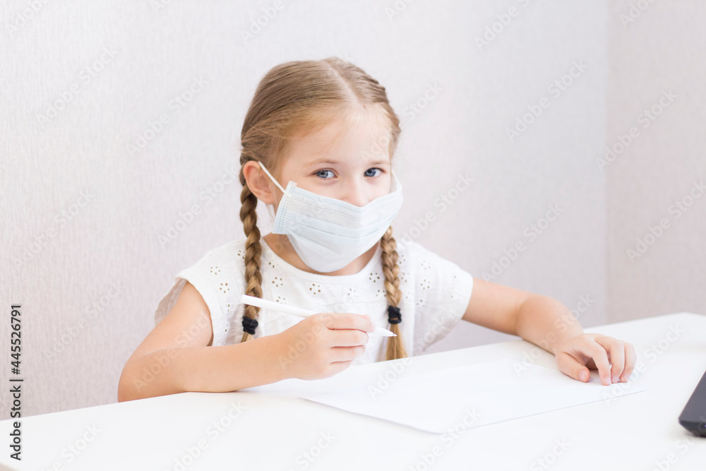 A LITTLE GIRL IN A MASK SITS AT A TABLE AND DRAWS, WRITES. STUDENT. SCHOOL. THE FIRST OF SEPTEMBER. HOME QUARANTINE