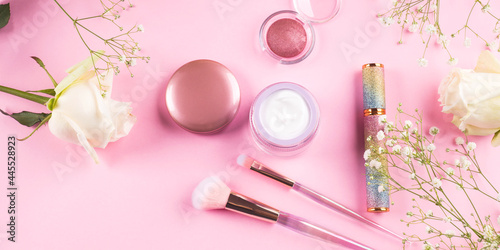 Trendy make up brushes with products on pink background with gypsophila flowers
