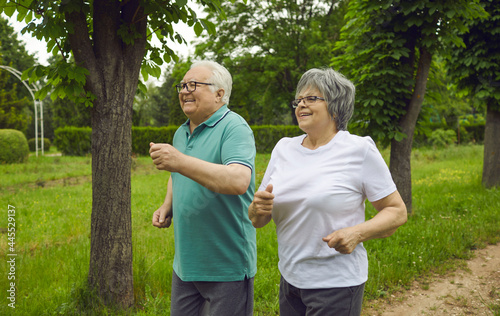Cheerful woman and man with gray hair in the park. Outdoor sports for seniors. Elderly sportive couple jogging in the park together in sportswear.