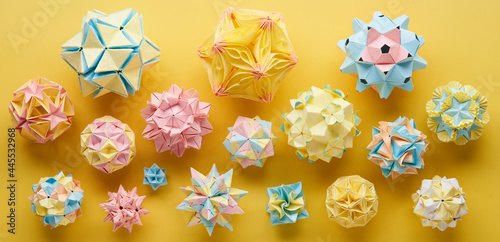Set of multicolor handmade modular origami balls or Kusudama Isolated on yellow background. Visual art, geometry, art of paper folding, paper crafts. Top view, close up, selective focus, copy space.