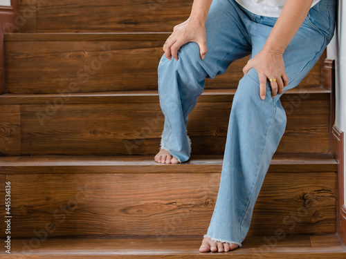 Woman stops for rest and leaning on wall for support while she cannot climb stairs with tingling legs. Concept of Guillain barre syndrome and numb legs disease or vaccine side effect photo