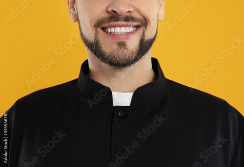 Priest wearing cassock with clerical collar on yellow background, closeup photo