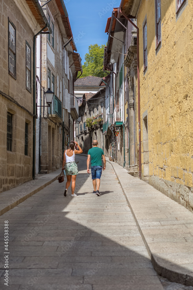 View at a old and narrow street with classic buildings on downtown Guimarães city, couple walking on background