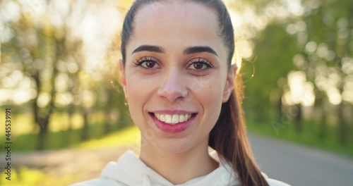 Close up shot of happy joyful Caucasian beautiful woman in good mood looking at camera and smiling standing on street in the morning. Young female with smile on face, outdoor workout, emotions concept photo