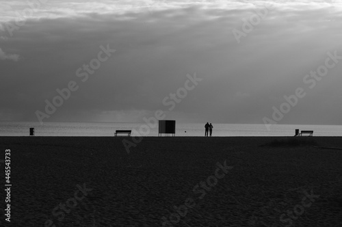 Black and white empty beach at the sea, silhouette of the benches and some people