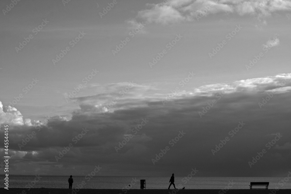 Black and white empty beach at the sea, silhouette of the benches and some people