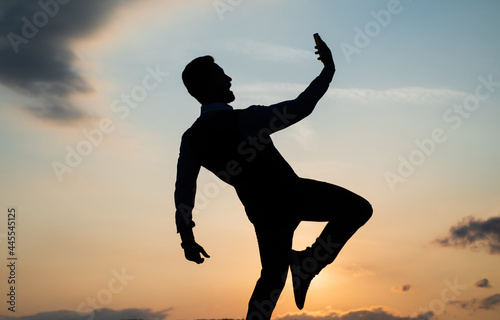 silhouette of guy making selfie on phone and make step in sense of freedom on sunrise sky, future