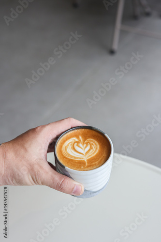 Closeup image of a man holding a white cup of coffee with latte art