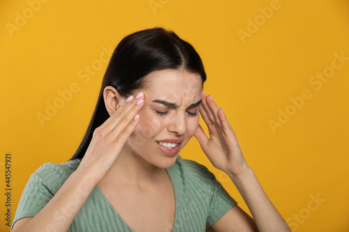 Woman suffering from migraine on yellow background © New Africa