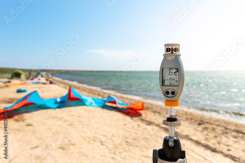 Close-up anemometer wind meter gadget against surf kite equipment on sand beach shore watersport spot on bright sunny day surfing tent campsite sea ocean coast. Fun adventure travel sport acitivity