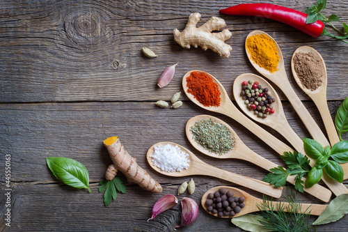 Composition of herbs and spices in wooden spoons on old boards background
