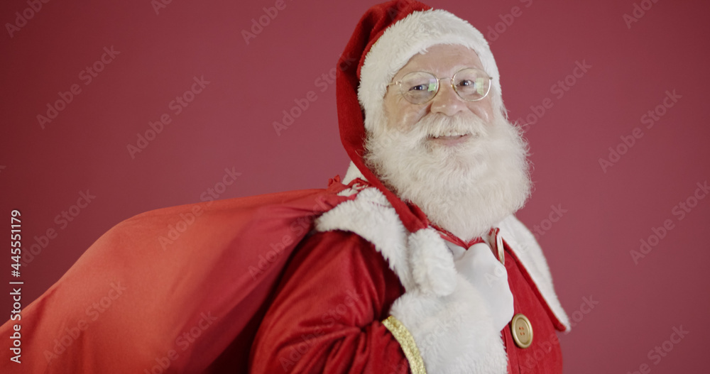 Real Santa Claus with a red background, wearing glasses, gloves and a hat looking side. Real Santa Claus with a red background, wearing glasses, gloves and a hat looking side.