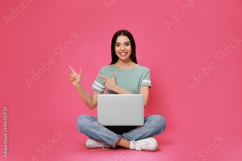 Young woman with modern laptop on pink background