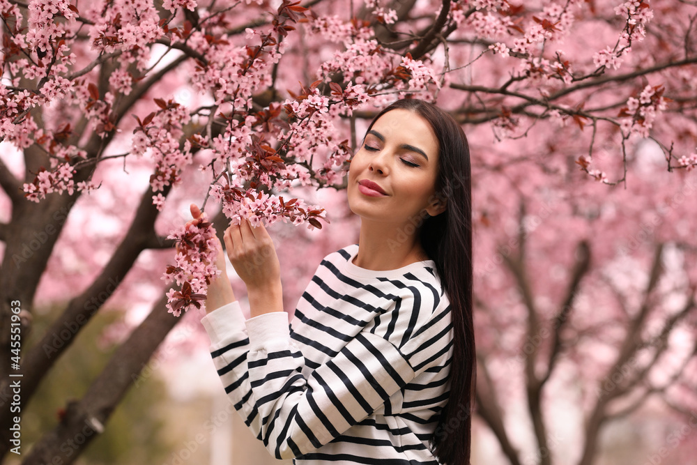 Pretty young woman near blooming tree in park. Spring look Pretty young woman near blooming tree in park. Spring look