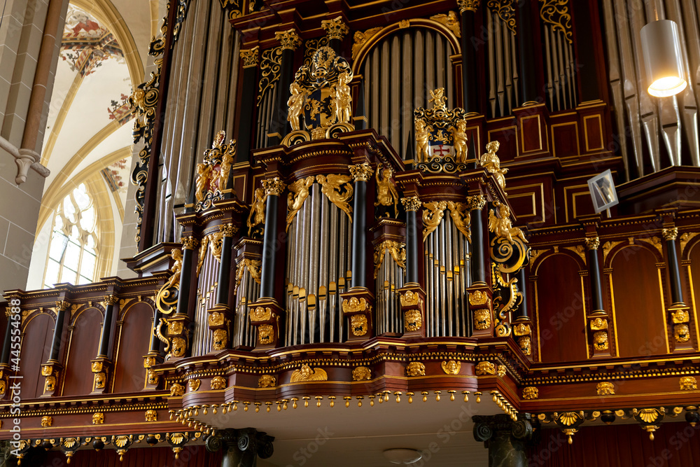Richly decorated church organ with golden ornaments on the metal pipe structure. Religious music instrument in cathedral.