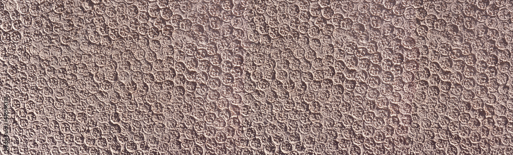 Abstrakter brauner Verputz mit Muster aus kleinen Kreisen an einer Wand im Sonnenlicht 