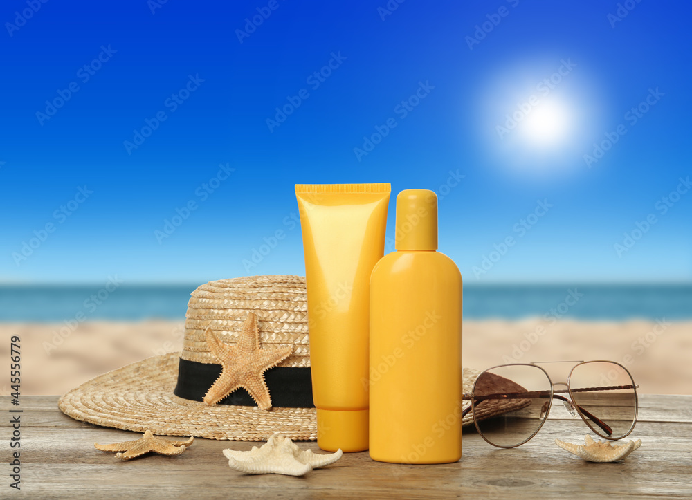 Skin sun protection products and beach accessories on wooden table against seascape. Space for design Skin sun protection products and beach accessories on wooden table against seascape. Space for design