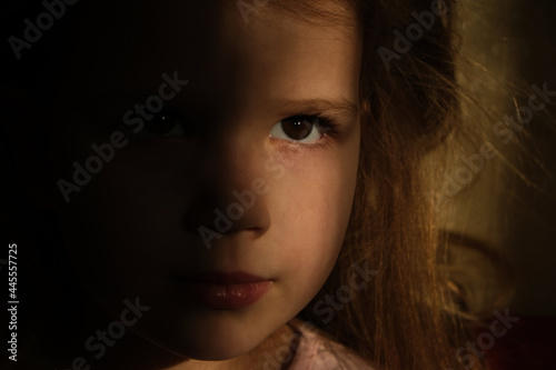 Little girl in dark side with shadow on face with blissful eyes looking dreaming or praying. Soft focus. Indoor portrait with natural light coming from a window