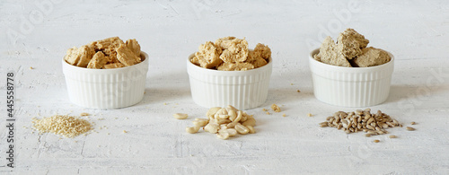 three bouls with halva of sesame seeds, peanuts and sunflower seeds  and the  seeds lie nearly on white background photo