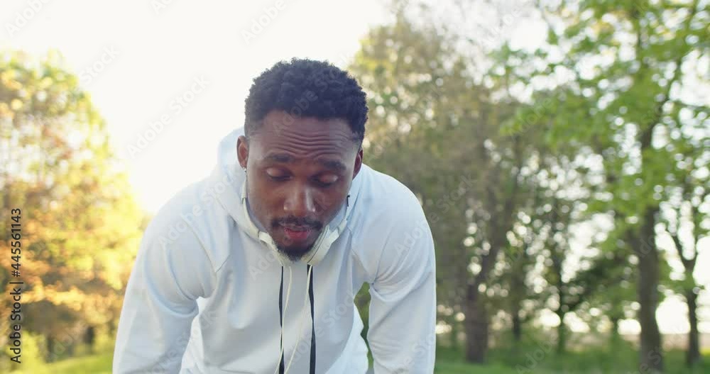 Close up of African American young handsome guy athlete putting headphones on and begin running outdoors listening to music. Sporty lifestyle. Sport activity. Sportsman working out, cardio workout Close up of African American young handsome guy athlete putting headphones on and begin running outdoors listening to music. Sporty lifestyle. Sport activity. Sportsman working out, cardio workout