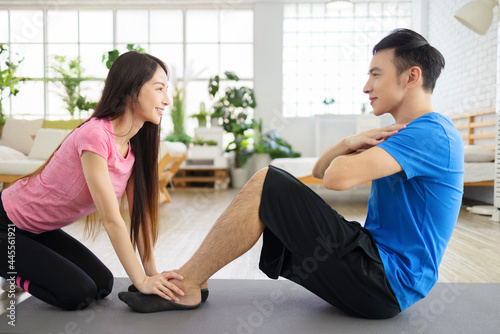 Young woman helping young man to do crunches at home .