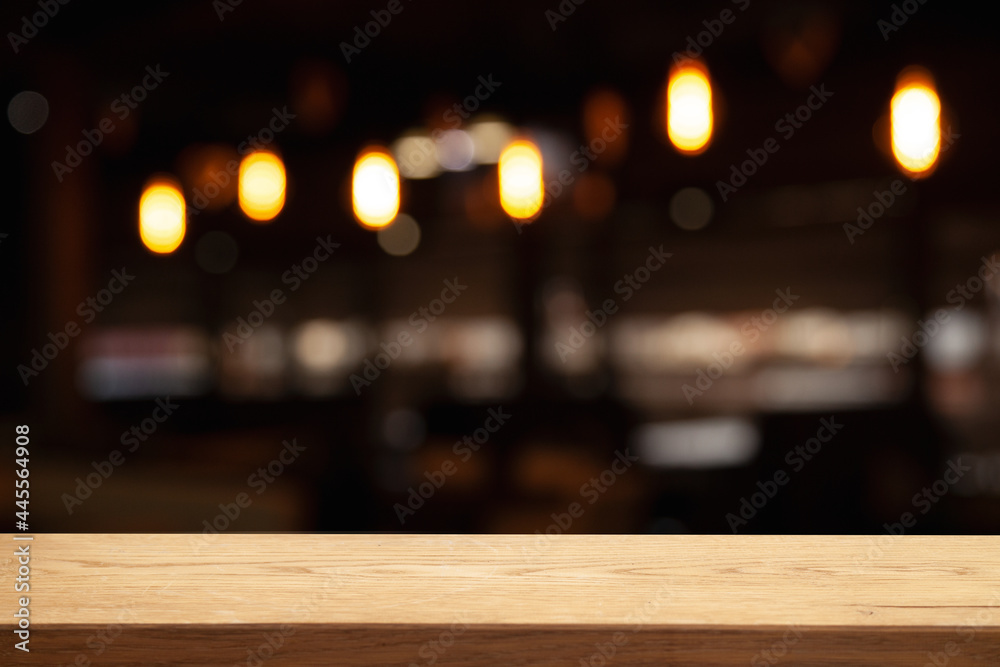 image of wooden table in front of abstract blurred background of lights of restaurant bar cafe