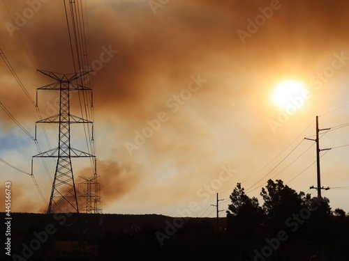 Large overland power lines leading toward the blue mountains with bush fire smoke haze across the setting sun.