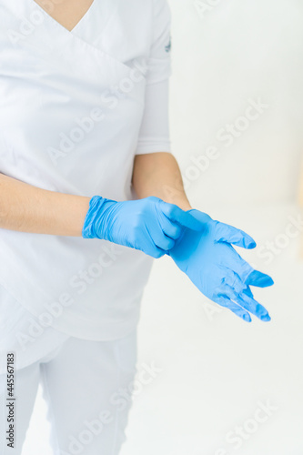 Medical concept. Nurse doctor surgeon dentist without face wear white costume puts on rubber disposable sterile blue gloves isolated on white soft blure background. Verical photo. Focus on hands,
