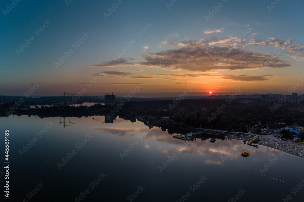Scenic aerial sunrise panorama with clouds reflecting in mirror water surface on wide river. Early morning, dawn in Kharkiv Zhuravlivskyy Hidropark from sky. Drone photography