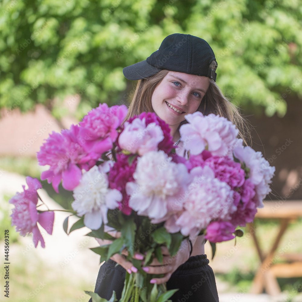 Beautiful and happy young girl in the summer with a beautiful bouquet of peonies in nature