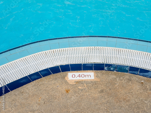 The edge of the pool with indication of the depth of the descent. Near the pool with clear blue water, the depth of the descent is 0.40 meters.