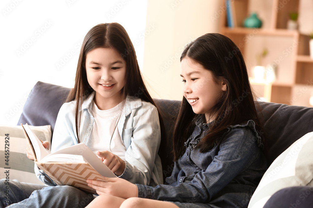 Cute Asian sisters reading book at home Cute Asian sisters reading book at home