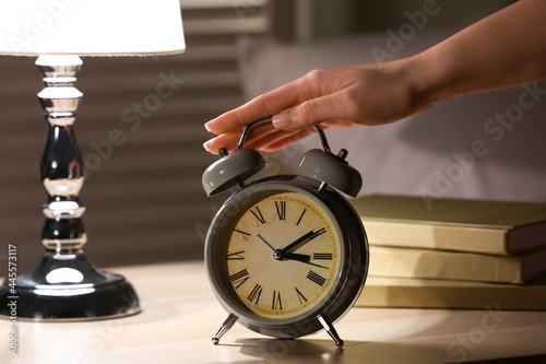 Woman turning off alarm clock on table at night