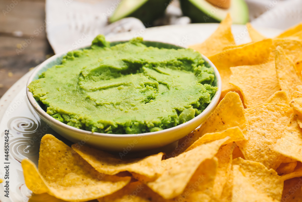 Bowl with tasty guacamole and nachos on table, closeup