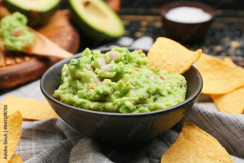 Bowl with tasty guacamole and nachos on table, closeup