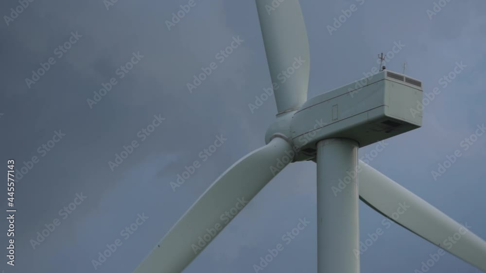 Grey contemporary energy source windmill with blades rotates under sky with dense stormy clouds on wind farm low angle shot. Sustainable clean energy concept. Grey contemporary energy source windmill with blades rotates under sky with dense stormy clouds on wind farm low angle shot. Sustainable clean energy concept.