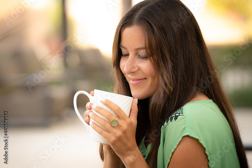 Beautiful Pretty Young Brunette Woman Drinking Coffee Outdoors in White Cup with Natural Soft Daylight at Mall Café Outside