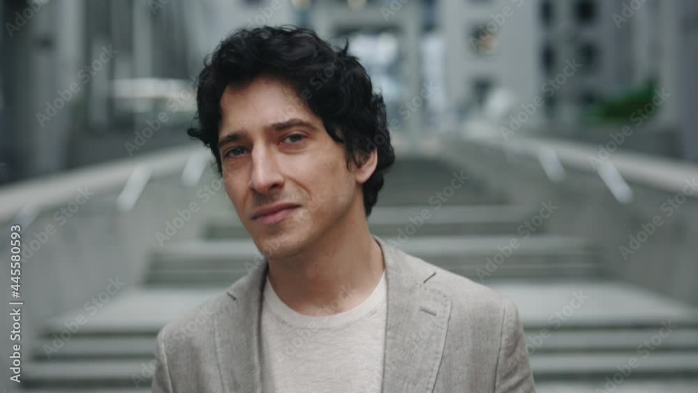 Smart and confident. Portrait view of the brunette caucasian business man looking at the camera while walking through the street with buildings at the background. Smart and confident. Portrait view of the brunette caucasian business man looking at the camera while walking through the street with buildings at the background.