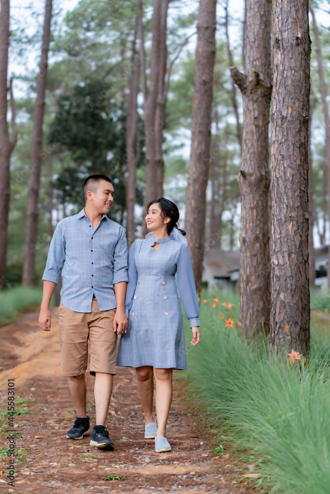 Portrait Pre Wedding of an Asian couple dressed in the same blue tones posing in a pine garden expressing their love in happiness behind an out-focused pine tree. Portrait Pre Wedding of an Asian couple dressed in the same blue tones posing in a pine garden expressing their love in happiness behind an out-focused pine tree.